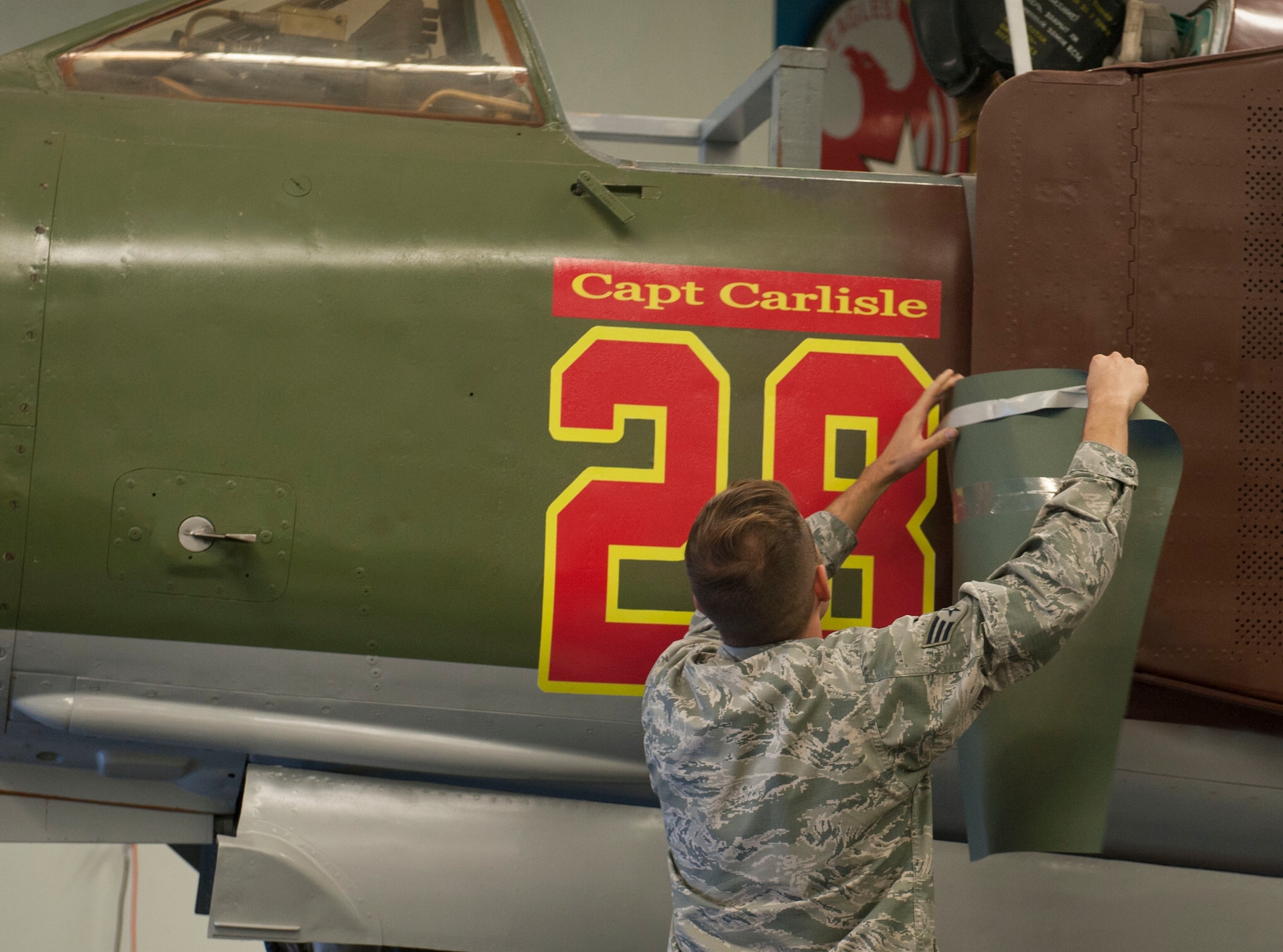 An Airman reveals the nickname of a MiG-23 during a dedication ceremony at the Threat Training Facility on Nellis Air Force Base, Nev., Oct. 17. The MiG-23 was dedicated to Gen. “Hawk” Carlisle, commander of Air Combat Command, in recognition of his time as the Chief of Weapons and Tactics and Flight Commander for the 4477th Test and Evaluation Squadron from 1986 to 1988.