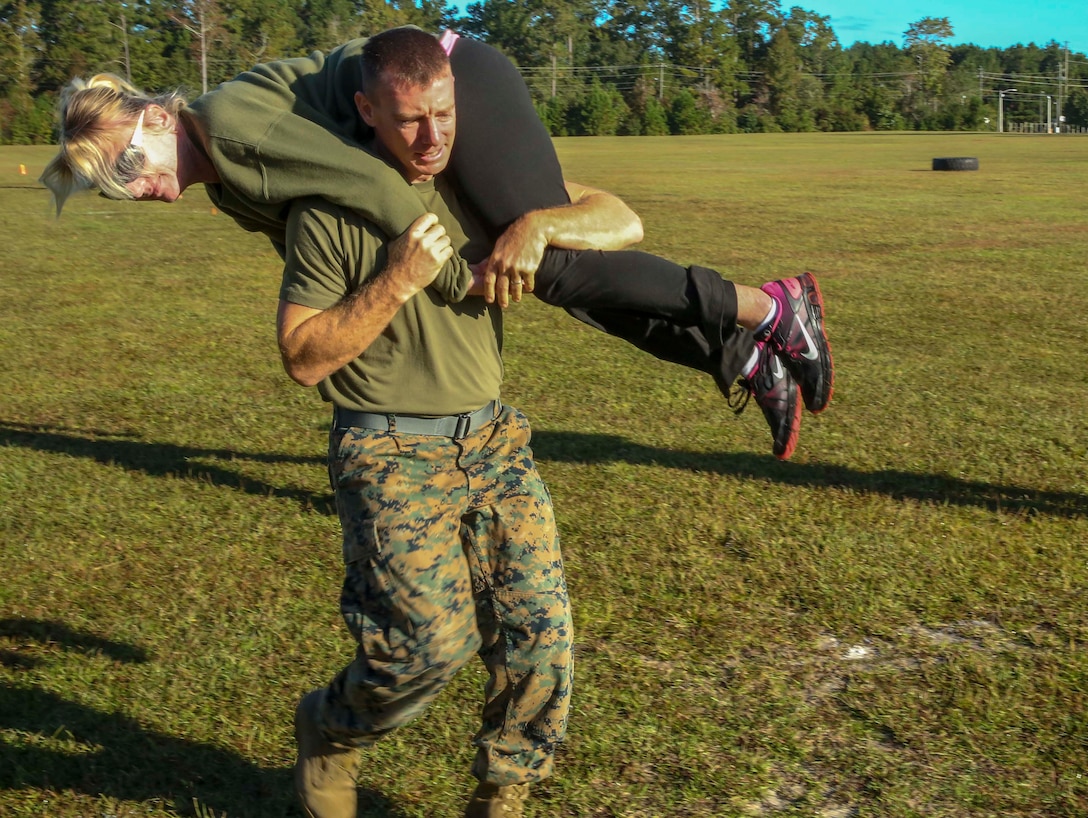 Master Sgt. Mathew McLaughlin, S-4 logistic chief, fireman carries his wife Renee McLaughlin during the J. Wayne Day combat fitness event at Camp Johnson on Marine Corps Base Camp Lejeune, Oct. 21. J. Wayne Day is a day where military spouses participate in activities representing what their Marines take part in on a constant basis.