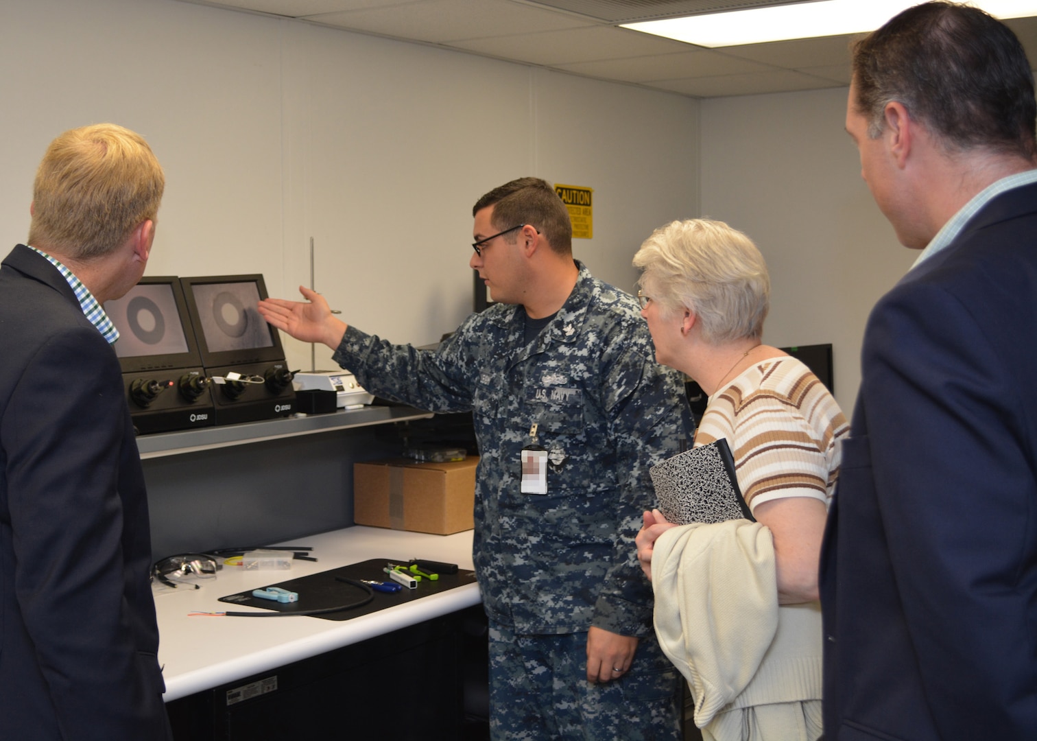 Petty Officer 1st Class Andrew Leigh (2nd from left) demonstrates to Mr. Craig Collier, (L) Ms. Vickie Plunkett and Mr. Andrew Warren who are professional staff members on the House Armed Services Committee, how Sailors at Southeast Regional Maintenance Center (SERMC) test, clean and repair fiber optic cable. The 2M (Miniature/Micro-miniature) shop at SERMC can inspect, repair, fabricate and troubleshoot fiber optic cable onboard all applicable classes of U.S. Navy surface ships. (Photo by Scott Curtis)