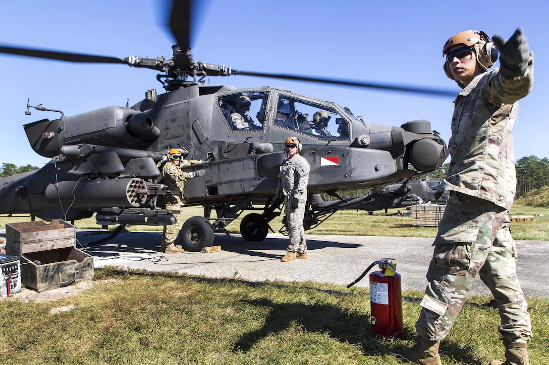 A soldier signals to an approaching AH-64 Apache helicopter at a forward arming and refueling point while another helicopter receives fuel during an aerial gunnery exercise at Fort Stewart, Ga., Oct. 22, 2016. Army photo by Spc. Scott Lindblom