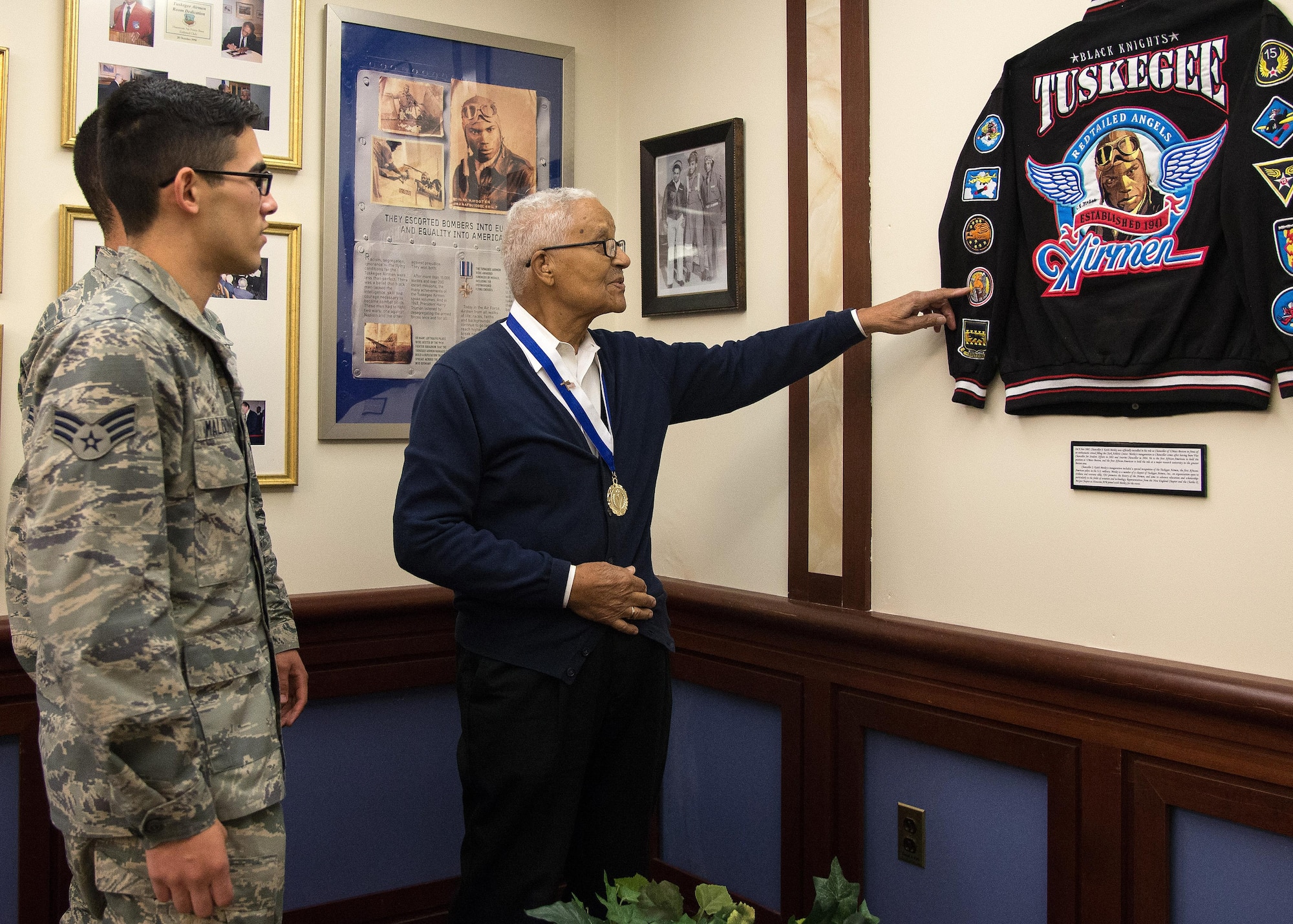 Retired Col. Charles E. McGee, an original Tuskegee Airman, points to patches on a Tuskegee Airmen jacket that is displayed at the Minuteman Commons on base Oct. 27, while Senior Airman Alfredo Maldonado, right, and Airman 1st Class Quinton Coke, both personnelist with the 66th Force Support Squadron, look on. McGee met with Airmen and discussed Air Force history and challenged each Airmen to believe in themselves. (U.S. Air Force photo by Mark Herlihy)   
