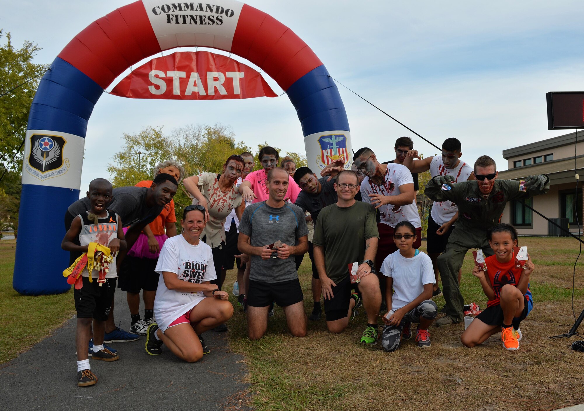 The top male and female runners of the Fear the Running Dead race kneel with zombiefied Air Commandos at Hurlburt Field, Fla., Oct. 27, 2016. Race participants won trophies and gift certificates for being the fastest runners and the best dressed zombies. (U.S. Air Force photo by Senior Airman Andrea Posey)