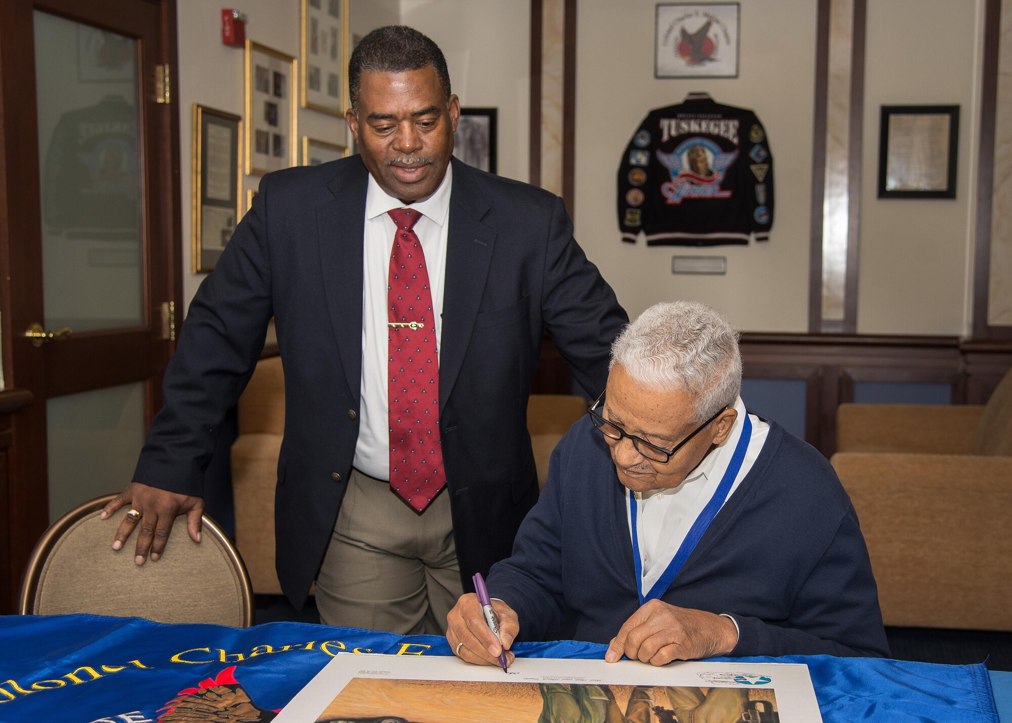 Retired Col. Charles E. McGee, an original Tuskegee Airman, signs a lithograph during a visit to the Minuteman Commons Oct. 27, while Galen Williams, the local Col. Charles E. McGee Tuskegee Airmen Chapter president, looks on. McGee held an impromptu meeting this week with Airmen prior to speaking at an event in Boston co-hosted by the New England Tuskegee Airmen Chapter and the local chapter bearing his name.