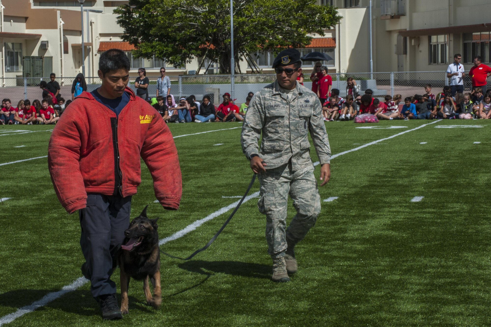 U.S. Air Force Senior Airman Juan Salinas, 18 Security Forces Squadron military working dog handler with military working dog Ayila, demonstrate escorting with Shitetsu Hirata, 18 SFS assistant trainer at Ryukyu Middle School at Kadena Air Base, Japan, for Red Ribbon Week Oct. 21, 2016. Red ribbon week first began after the murder of a Drug Enforcement Administration agent, Enrique Camarena, to raise awareness about the destruction and death caused in the wake of rampant drug abuse. (U.S. Air Force photo by Airman 1st Class Nick Emerick/Realeased) 