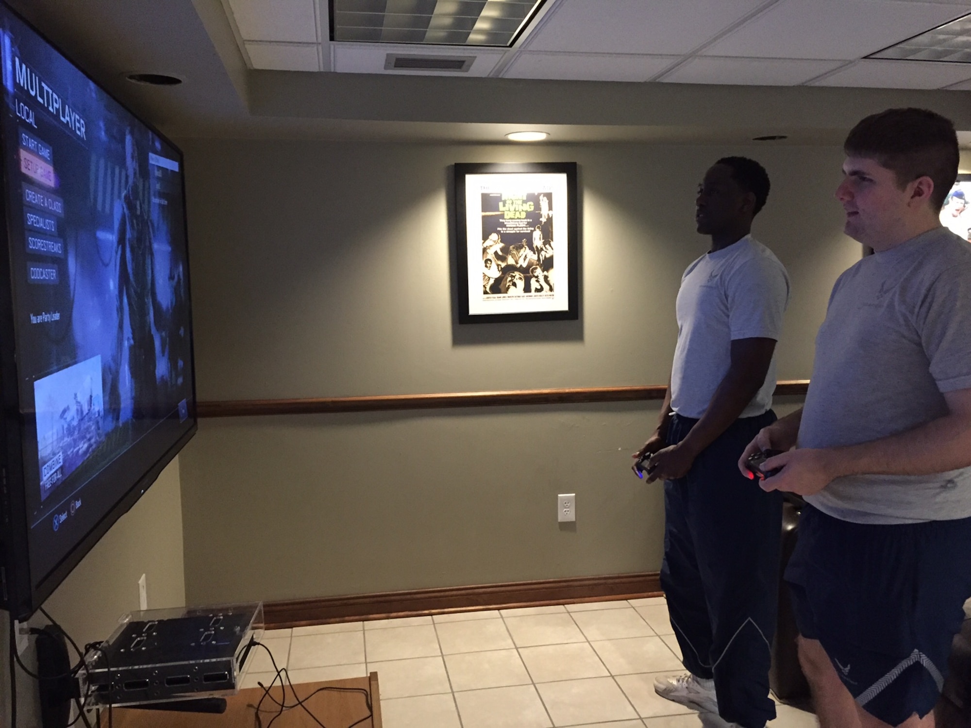 Airman 1st Class Wesley Cassius of the 88th Security Forces Squadron, left, and Airman 1st Class Charles Williamson, an air traffic controller in the 88th Operations Support Squadron, enjoy playing PlayStation on one of the huge new smart TV screens recently installed in the dayroom of Bldg. 1216, Kittyhawk Center, Area A. Gathering in the day room builds esprit de corps. (Skywrighter photo/Amy Rollins)