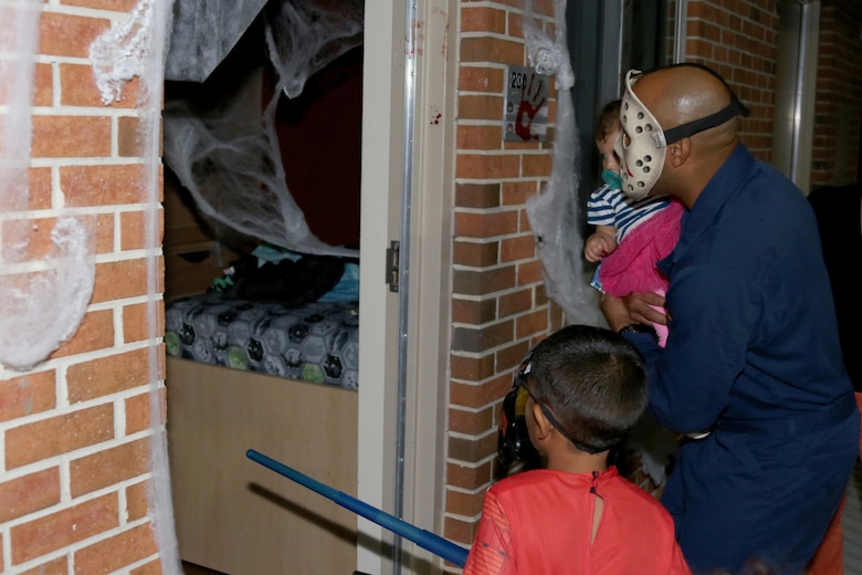 Sgt. Maj. Miguel Betancourt III, right, leads his family into a Halloween-themed barracks room during a Haunted Barracks event aboard Marine Corps Air Station Cherry Point, N.C., Oct. 28, 2016. Marine Wing Headquarters Squadron 2 hosted the event to give Marines living in the barracks an opportunity to celebrate Halloween with other MWHS-2 Marines and their families. Children went door-to-door with their parents and received candy from the Marines. Betancourt is the MWHS-2 sergeant major.