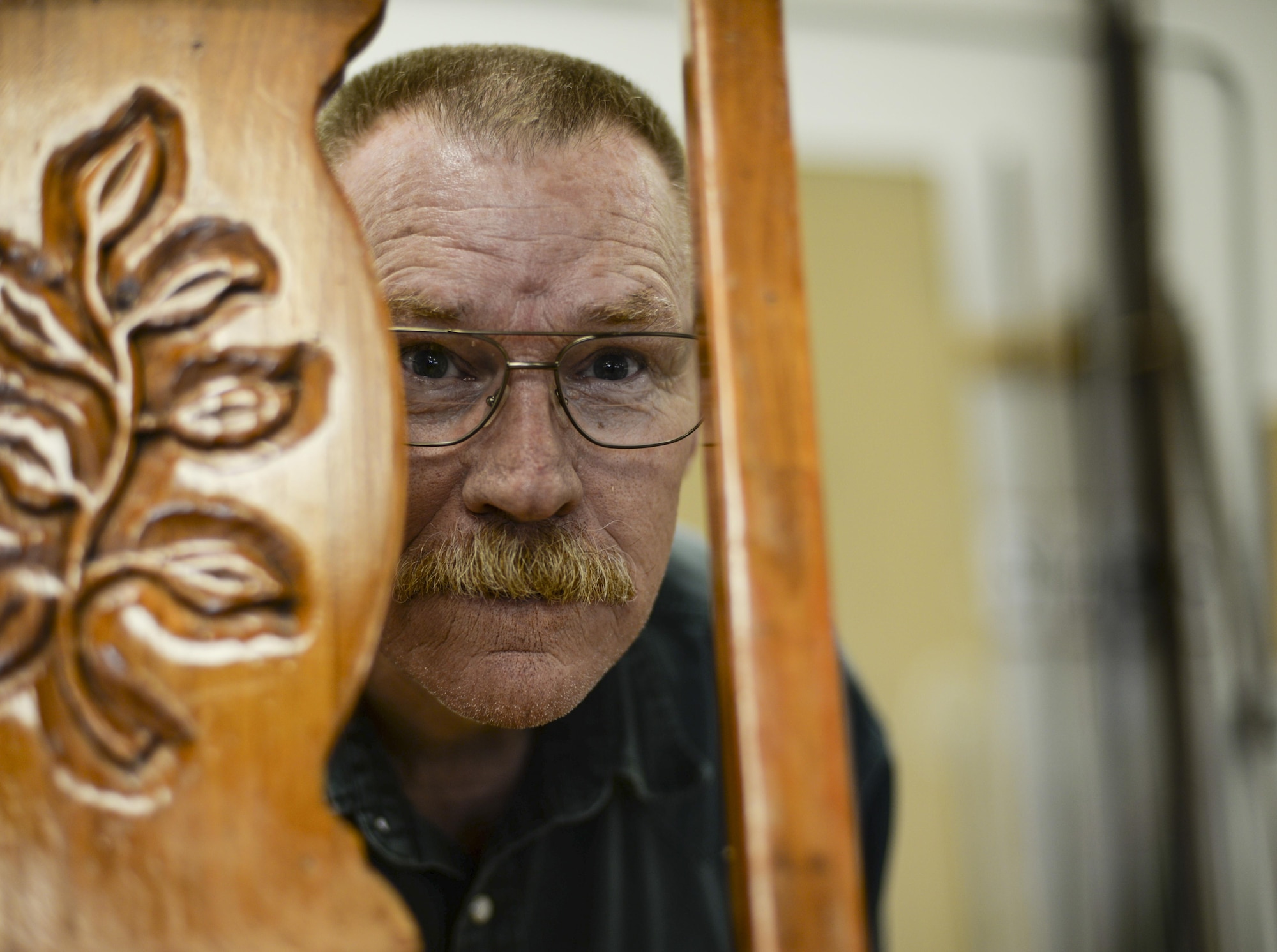 Joe, the 49th Force Support Squadron Wood Shop supervisor, peers between the bars of an antique chair at Holloman Air Force Base, N.M. 9 Aug. 2016. The Arts & Crafts Center houses a Frame Shop, Ceramics Studio, Embroidery Shop, Engraving & Trophy Shop and the Wood Shop. (Last names are being withheld due to operational requirements. U.S. Air Force photo by Airman Alexis P. Docherty) 