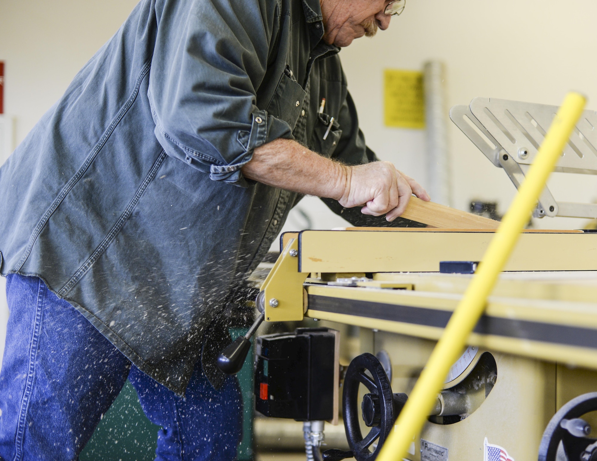 Joe, the 49th Support Squadron Wood Shop supervisor, pushes a board of redwood through a table saw at Holloman Air Force Base, N.M. 23 Aug. 2016. The Wood Shop is open to craftsmen and hobbyists of all skill levels, from beginner to expert. (Last names are being withheld due to operational requirements. U.S. Air Force photo by Airman Alexis P. Docherty) 

