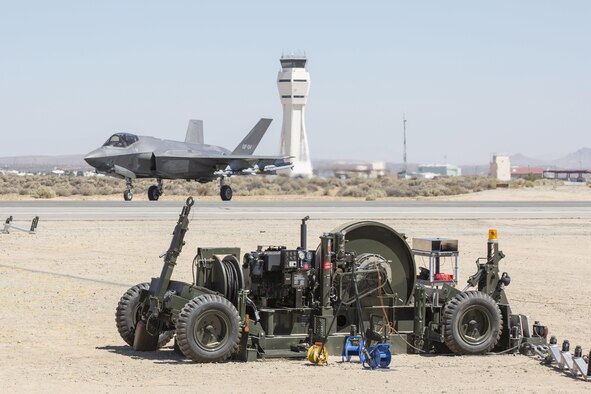 A Civil Engineer Maintenance Inspection and Repair Team, or CEMIRT, overhauled mobile aircraft arresting system, MAAS, is pictured on the runway with the approaching F-35A Joint Strike Fighter preparing to capture the cable with its tail hook. The MAAS was installed by the 820th Rapid Engineer Deployable Heavy Operations Repair Squadron Engineers from Nellis Air Force Base, Nevada, and used during testing at Edwards Air Force Base, California. (Courtesy photo by Mike Jackson/Lockheed Martin)