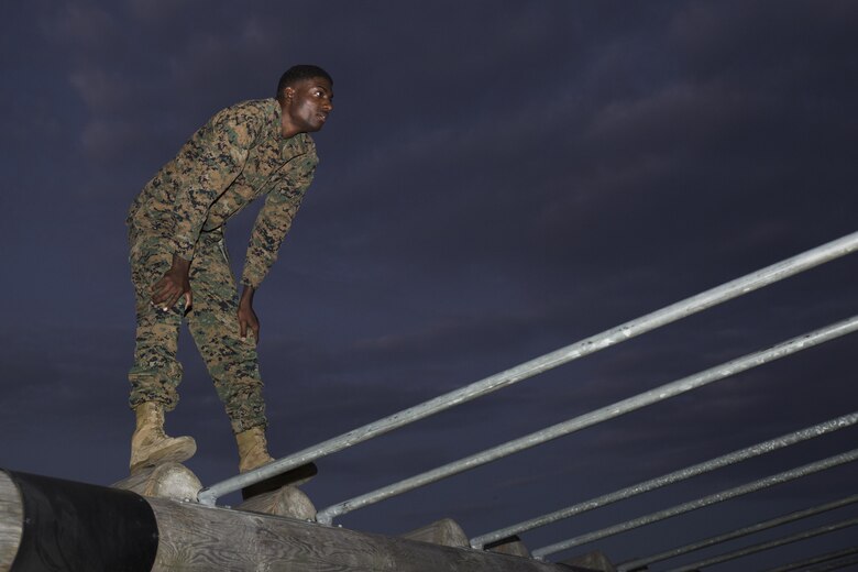 Lance Cpl. Kwesi Thomas, armorer with Marine Aircraft Group 12, waits for a bowl of water while standing on an obstacle within the obstacle course at Marine Corps Air Station Iwakuni, Japan. Marines with MAG-12 ran the obstacle course and received a Professional Military Education lesson on leadership as part of their physical training.  (U.S. Marine Corps photo by Lance Cpl. Abrego)