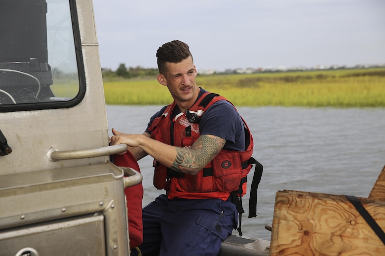 Seaman Gerald Ihnken, a U.S. Coast Guardsman stationed at USCG Station Oak Island, holds onto a railing as the trailerable aids to navigation boat leaves the pier at Oak Island, N.C., Aug. 31, 2016. U.S. Marines with Battlefield Surveillance Company, 2nd Intelligence Battalion, teamed up with the Coast Guardsmen to create a topographical layout of waterways that were previously unidentifiable. The new maps will correct navigation discrepancies such as off-station buoys or extinguished lights.  (U.S. Marine Corps photo by Cpl. Kaitlyn V. Klein)