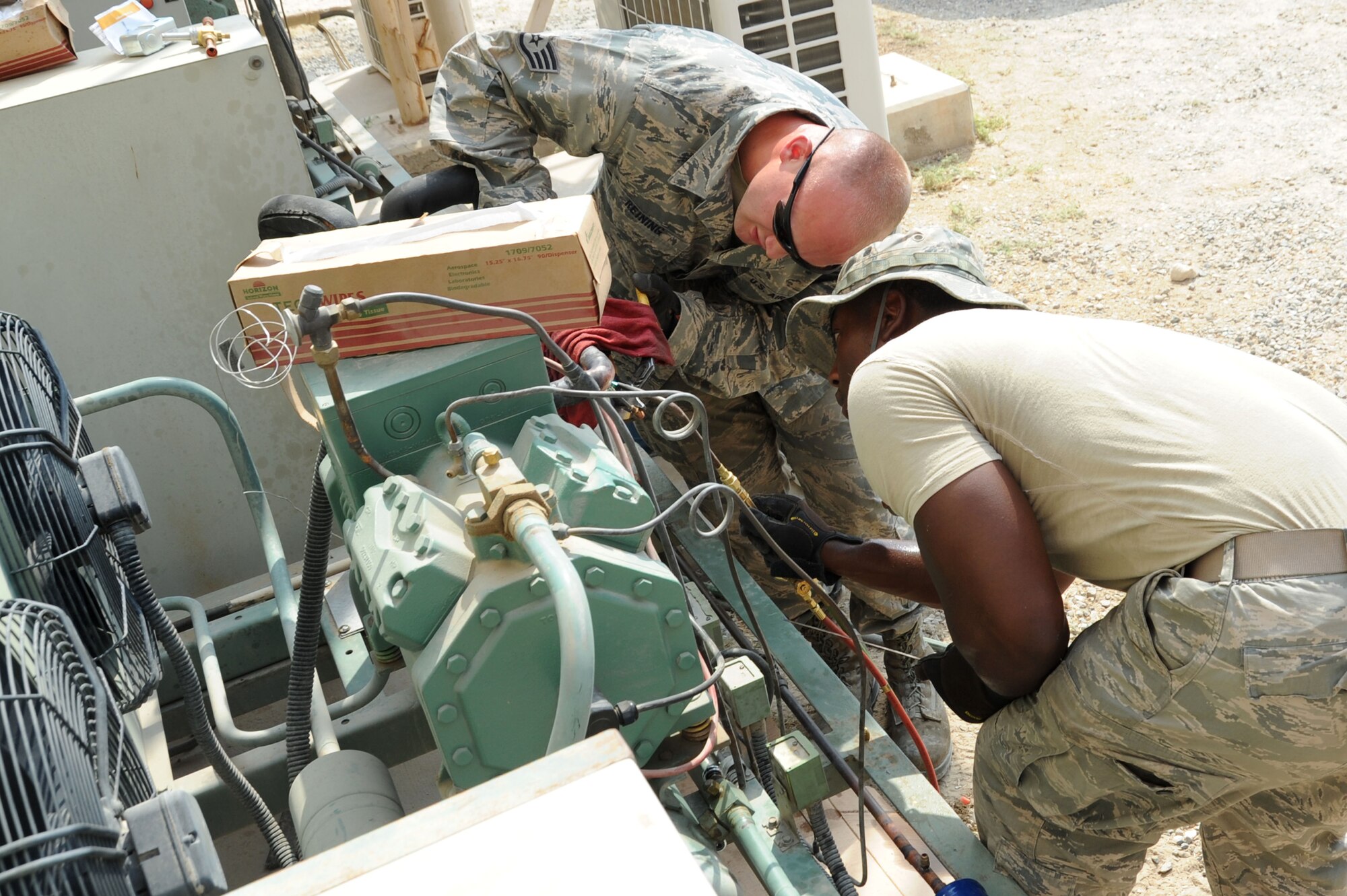 Staff Sgt. Corey Reining and Senior Airman Terrence Patton, 386th Expeditionary Civil Engineer Squadron heating, ventilation, and air conditioning technicians, perform maintenance on an A/C unit Sep. 2, 2016, at an undisclosed location in Southwest Asia. Due to extremely high temperatures, the 386 ECES HVAC shop must maintain the A/C units across the base more frequently to keep them at their optimal performance levels. (U.S. Air Force photo/Senior Airman Zachary Kee)