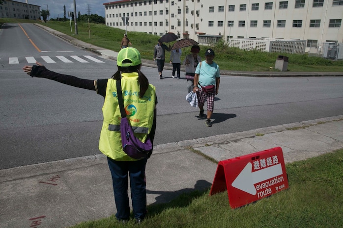 A volunteer directs Okinawa residents along the evacuation route during a tsunami evacuation drill Sept. 4 on Camp Foster, Okinawa, Japan. The drill was arranged to familiarize Okinawa residents with the evacuation route. In the event of a tsunami, Okinawa residents would follow the evacuation route through Camp Foster to higher ground. (U.S. Marine Corps Photo by Cpl. Brittany A. James/ Released)