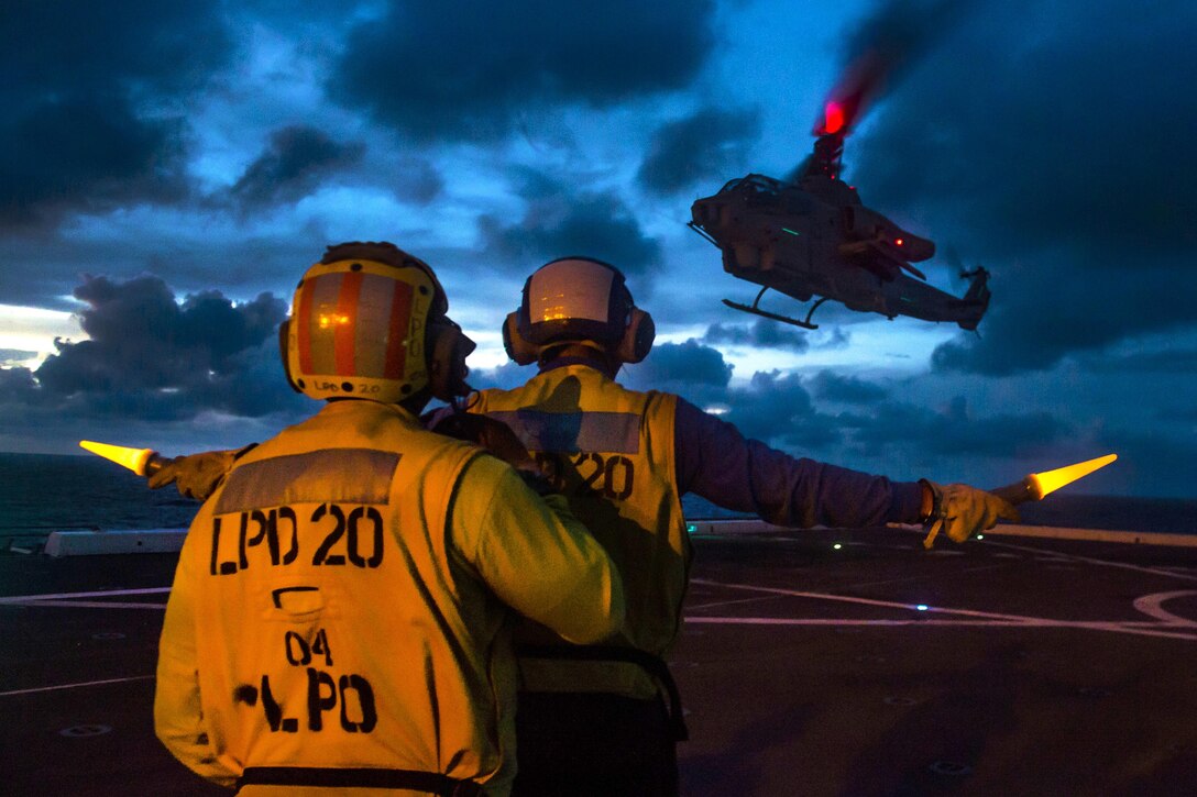 Navy Petty Officer 1st Class Patrick Henry, foreground, braces Seaman Andrew Jerauld as he signals to an AH-1W Super Cobra helicopter landing on the flight deck of the USS Green Bay in the Pacific Ocean, Sept. 5, 2016. The ship is in the U.S. 7th Fleet area of operations to support security and stability in the Indo-Asia-Pacific region. The helicopter is assigned to Marine Medium Tiltrotor Squadron 262. Navy photo by Petty Officer 3rd Class Patrick Dionne