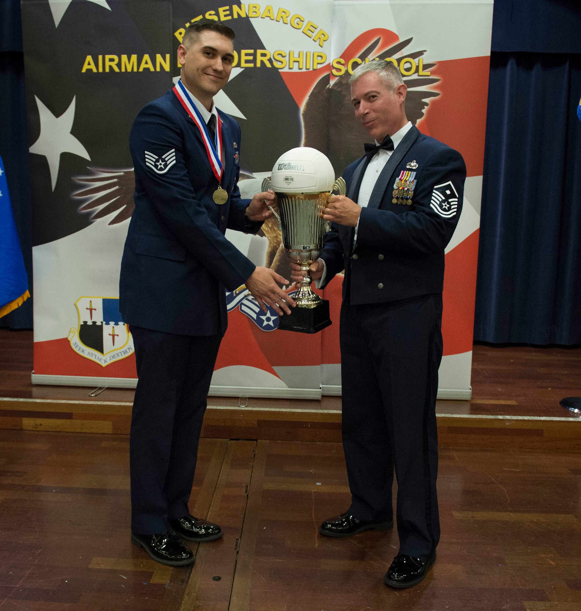 U.S Air Force Master Sgt. Bryon Hambacker, 726th Air Mobility Squadron first sergeant, right, hands a trophy to Staff Sgt. Cameron Gunnels, 52 Security Forces Squadron base defense operations center controller, left, during a Pitsenbarger Airman Leadership School graduation at Club Eifel on Spangdahlem Air Base, Germany, Aug. 25, 2016. The trophy exchange occurs when an ALS class defeats senior NCOs in a rivalry volleyball game held during the last two weeks of an ALS course. (U.S. Air Force photo by Airman 1st Class Preston Cherry/Released)