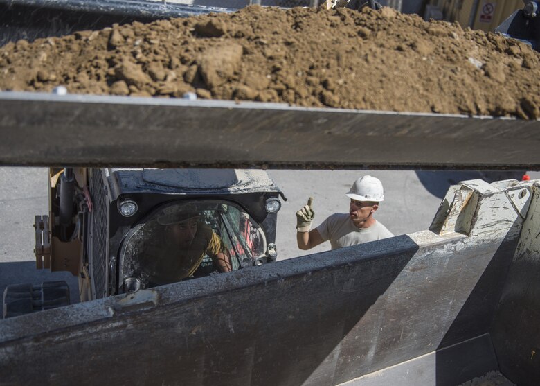 Staff Sgt. Casey Epps, 455th Expeditionary Civil Engineer Squadron pavements and equipment technician, assists Senior Airman Bobby Rayscales Jr., 455th ECES engineer assistant, as he plows dirt, Bagram Airfield, Afghanistan, Sept. 7, 2016. The construction area will be the site of a new drainage system located at the passengers terminal and will help collect excess water and precipitation. (U.S. Air Force photo by Senior Airman Justyn M. Freeman)