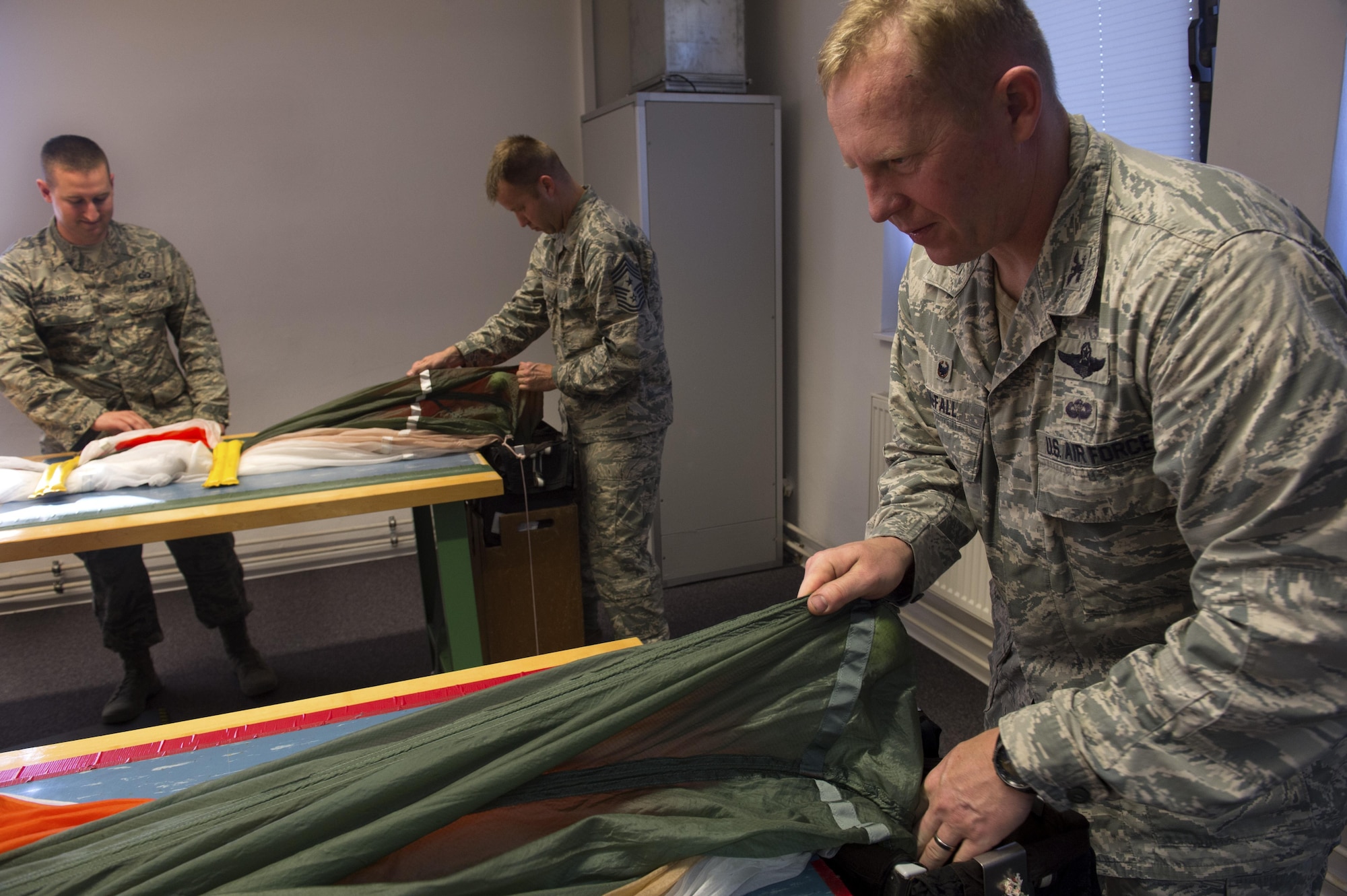U.S. Air Force Col. Joseph McFall, 52nd Fighter Wing commander, center, and Chief Master Sgt. Edwin Ludwigsen, 52nd Fighter Wing command chief, center left, pack training parachutes during a Saber leadership “out and about” at the parachute shop on Spangdahlem Air Base, Germany, Sept. 8, 2016. The event lets the 52nd FW commander and command chief get a hands on experience at Saber work centers in an effort to better understand the duties of Airmen at Spangdahlem. (U.S. Air Force photo by Airman 1st Class Preston Cherry/Released)