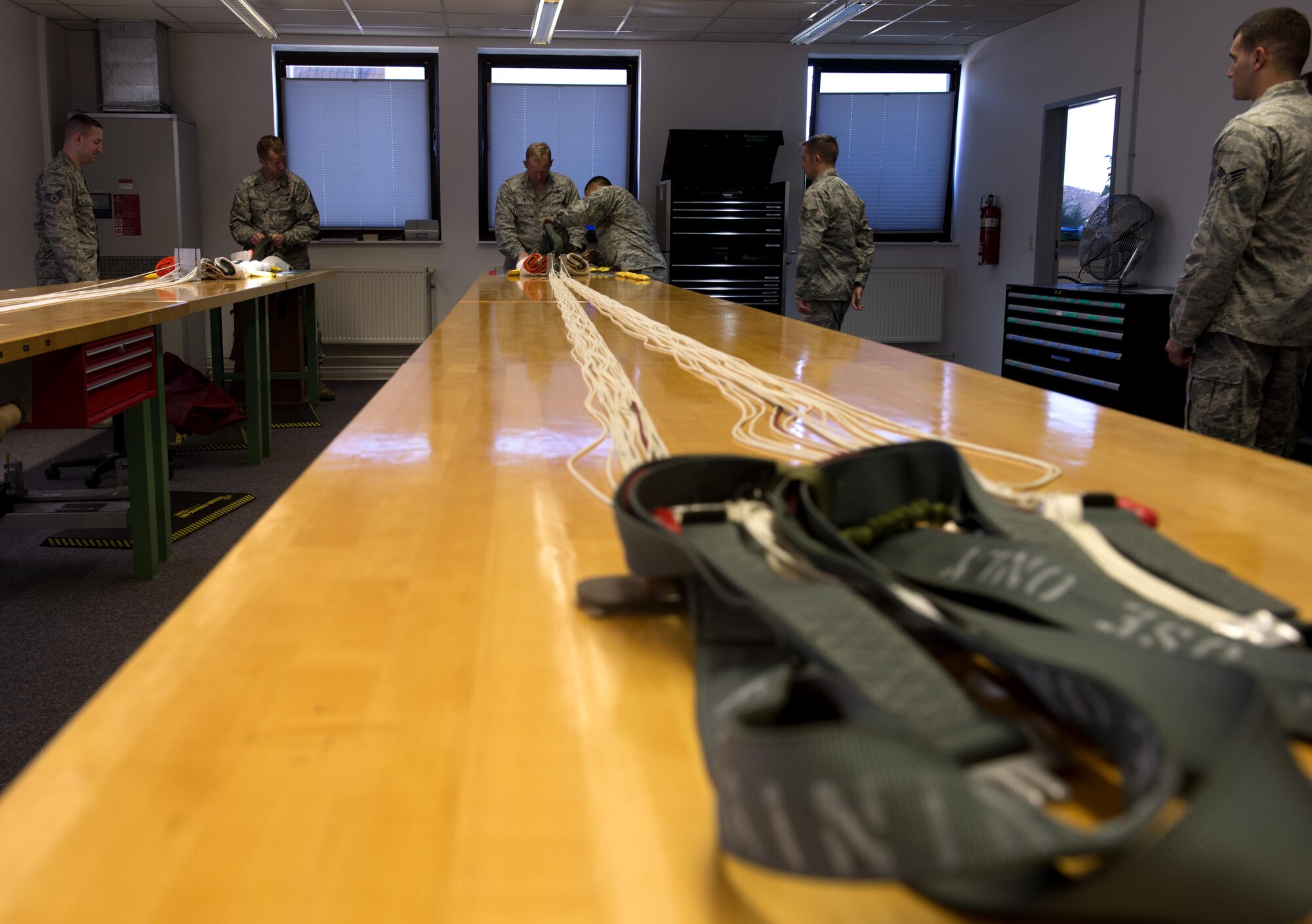 U.S. Air Force Col. Joseph McFall, 52nd Fighter Wing commander, center, and Chief Master Sgt. Edwin Ludwigsen, 52nd FW command chief, center left, pack training parachutes during a Saber leadership “out and about” at the parachute shop on Spangdahlem Air Base, Germany, Sept. 8, 2016. The event lets the 52nd FW commander and command chief get a hands on experience at Saber work centers in an effort to better understand the duties of Airmen at Spangdahlem. (U.S. Air Force photo by Airman 1st Class Preston Cherry/Released)