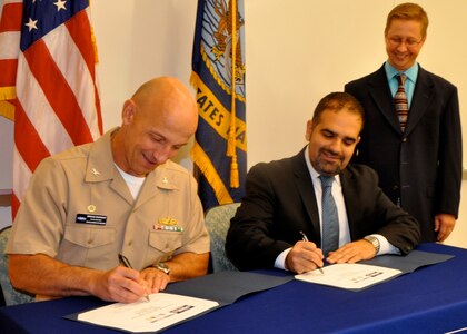 DAHLGREN, Va. (Sept. 7, 2016) - Capt. Brian Durant and Amit Kapoor sign an exclusive license agreement authorizing First Line Technology LLC to manufacture Navy patented lifesaving decontamination technology for warfighters and first responders. The 'Dahlgren Decon' decontamination solution - developed to defend U.S. troops against chemical, biological, and radiological agents - is protected under several patents by Naval Surface Warfare Center Dahlgren Division (NSWCDD). Durant, NSWCDD commanding officer, and Kapoor, First Line Technology president, emphasized the importance of the technology transfer that will equip first responders across the nation with technology to defend the public from hazardous threats. "This is the home run of technology transfer and doesn't happen without a lot of contributors," said Chris Hodge, NSWCDD scientist and Dahlgren Decon inventor, standing. Hodge and his team worked for more than a decade to develop and test this revolutionary response to chemical and biological warfare agents.