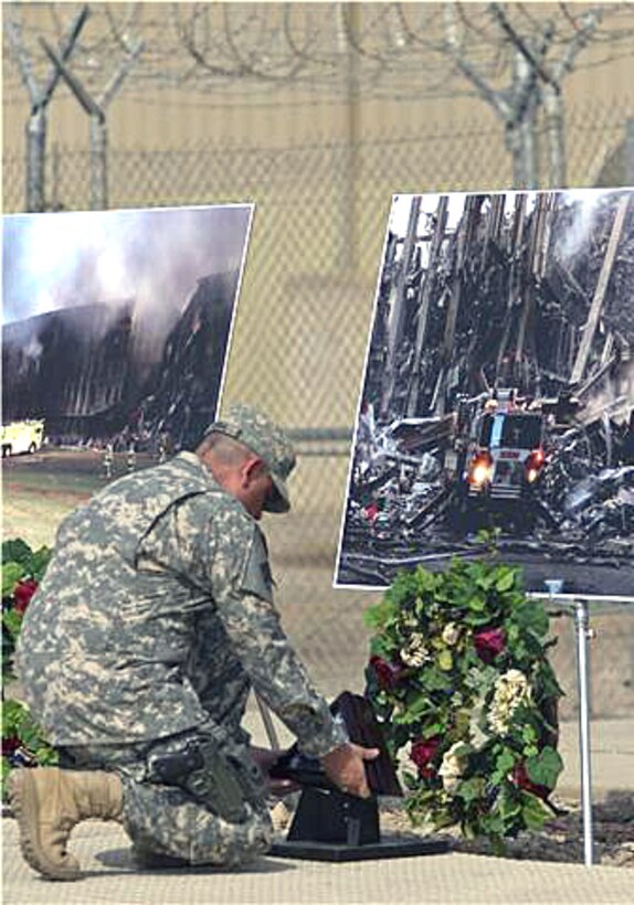 Army Command Sgt. Maj. John Gioia kneels down to place a flag that was flown at ground zero in front of a 9/11 photo memorial during the Patriot Day Observance at Camp Liberty, Iraq, Sept. 11, 2008. Gioia was the senior enlisted advisor for the 4th Infantry Division, Multinational Division Baghdad. Army photo by Staff Sgt. Brock Jones