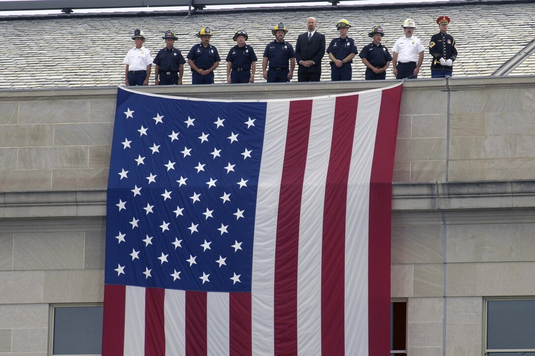 During ceremonies dedicating the Pentagon Memorial, representatives of police and firefighting units who were the first to respond to the 9/11 terrorist attack on the Pentagon, stand at the top of a large American flag suspended from the roof of the Pentagon, Sept. 11, 2008, just as they stood seven years earlier. DoD photo by R. D. Ward
