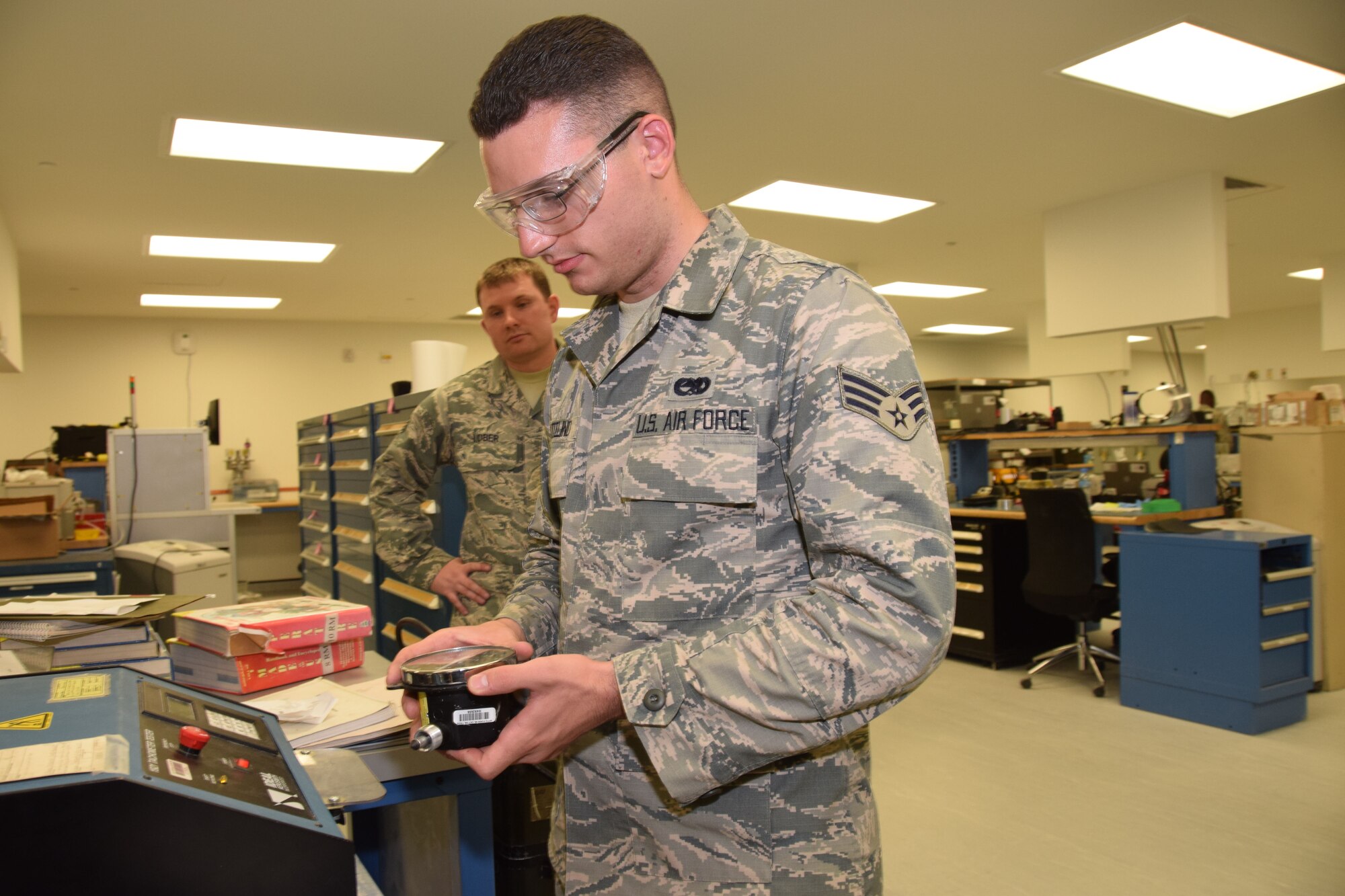 Senior Airmen Eric Vetelino (foreground) and Staff Sgt. Jacob Lober (background),  379th Expeditionary Expeditionary Maintenance Squadron Precision Measurement Equipment Laboratory craftsmen, work with a handheld tachometer belonging to a BAK12E32A aircraft arresting system Aug. 24, 2016, Al Udeid Air Base, Qatar. The handheld tachometer is used with the BAK123E2A and gives the user a reading of how fast the system's reel is spinning in revolutions per minute. (U.S. Air Force photo/Technical Sgt. Treviño/Released)