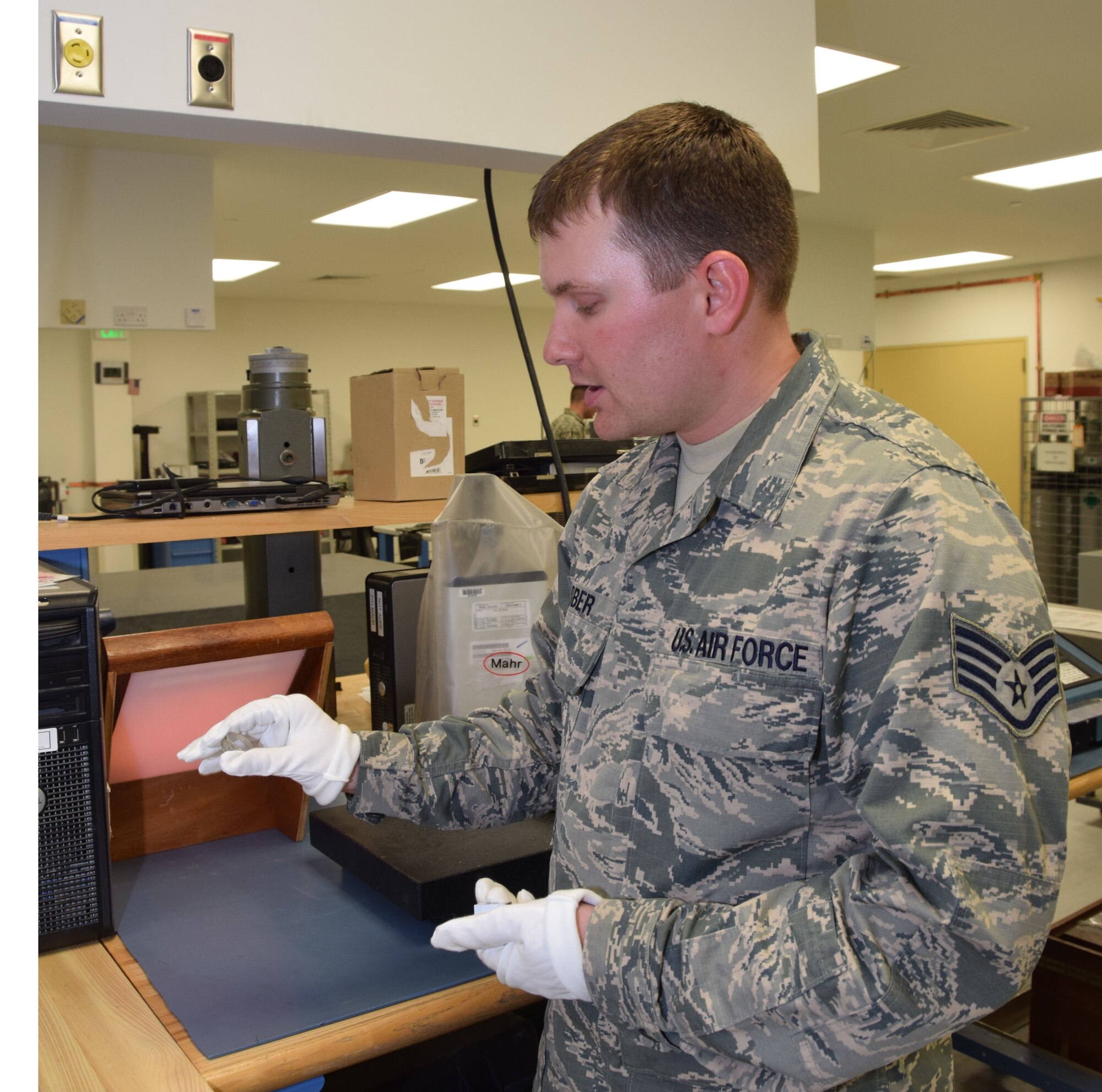 Staff Sgt. Jacob Lober,  379th Expeditionary Expeditionary Maintenance Squadron Precision Measurement Equipment Laboratory craftsman, wears gloves to hold a small clear piece called an optical flat  Aug. 24, 2016, Al Udeid Air Base, Qatar.  Lober wears the gloves to prevent any moisture from his hands touching the piece, which will ruin the flat. (U.S. Air Forc e photo/Technical Sgt. Carlos J. Treviño/Released)