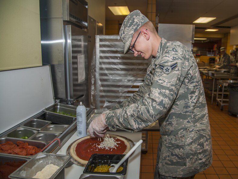A 5th Force Support Squadron Airman sprinkles cheese on a pizza at the new and improved Dakota Inn Dining Facility at Minot Air Force Base, N.D., Sept. 7, 2016. The DFAC cooks about 12 pizzas every day for lunch guests. (U.S. Air Force photo/Airman 1st Class Christian Sullivan)