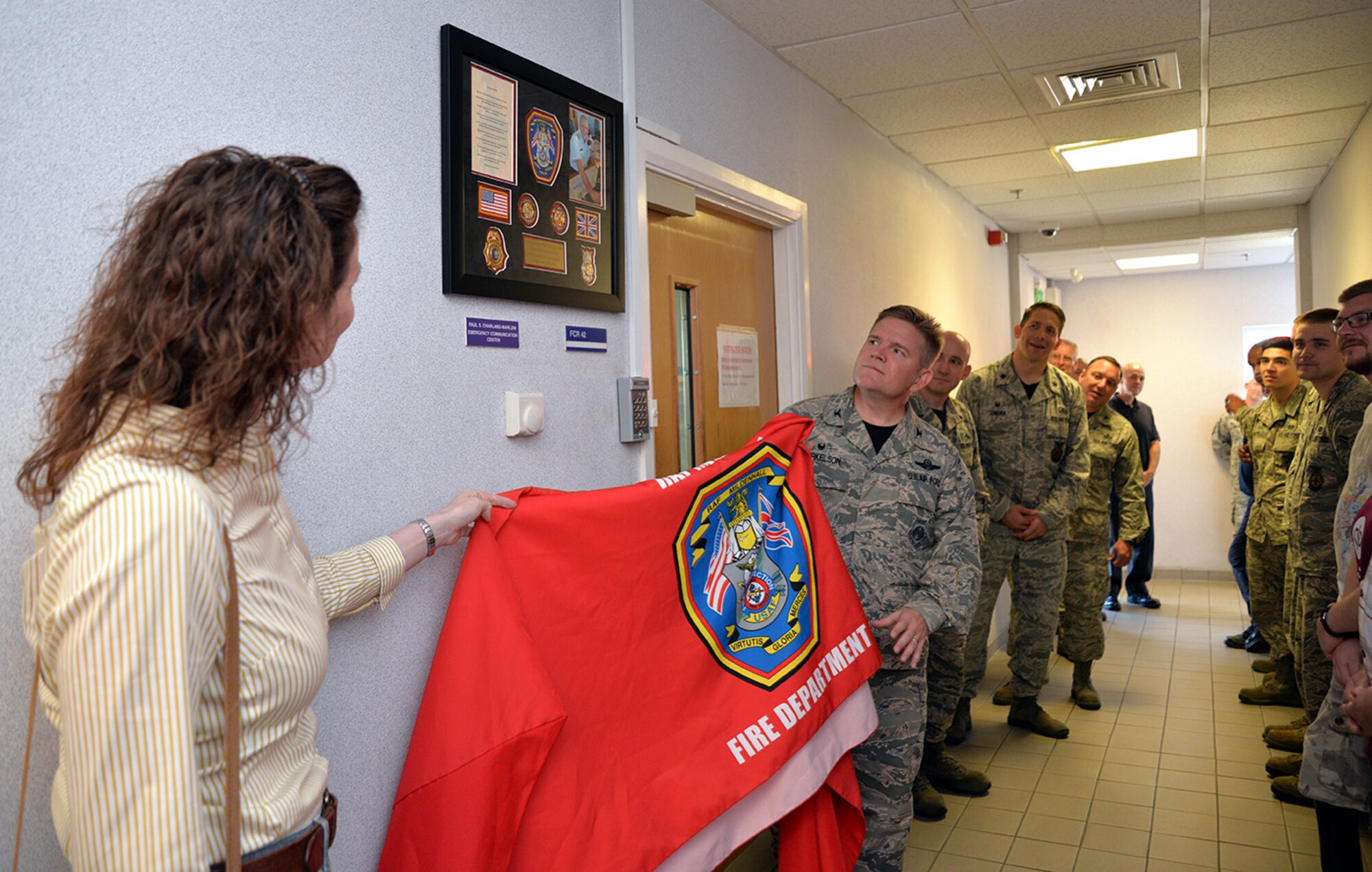 U.S. Air Force Col. Thomas D. Torkelson, second left, 100th Air Refueling Wing commander, and Michelle Charland-Marlow, wife of Paul Charland-Marlow, former 100th Civil Engineer Squadron Fire Department lead dispatcher, unveil a tribute to her late husband outside the emergency communication center Sept. 9, 2016, on RAF Mildenhall, England. Paul Charland-Marlow passed away March 30, 2016. The firefighters dedicated their alarm room to him so his memory would live on. (U.S. Air Force photo by Karen Abeyasekere)