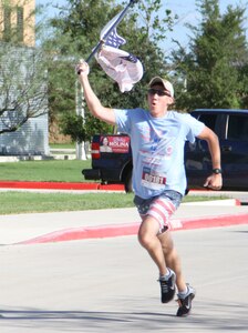 A runner crosses the finish line holding the American flag during the Texas A&M University-San Antonio 5K run for the 15th anniversary of the September 11, 2001 terrorist attacks on the World Trade Center buildings on Sept. 11, 2016, San Antonio. Texas A&M University-San Antonio was nominated to receive a sapling from the 9/11 Survivor Tree, which was the sole surviving tree that remained after the destruction of the World Trade Center buildings. (U.S. Army Reserve photo by Spc. Vincent Gonzalez 345th Public Affairs Detachment/Released)