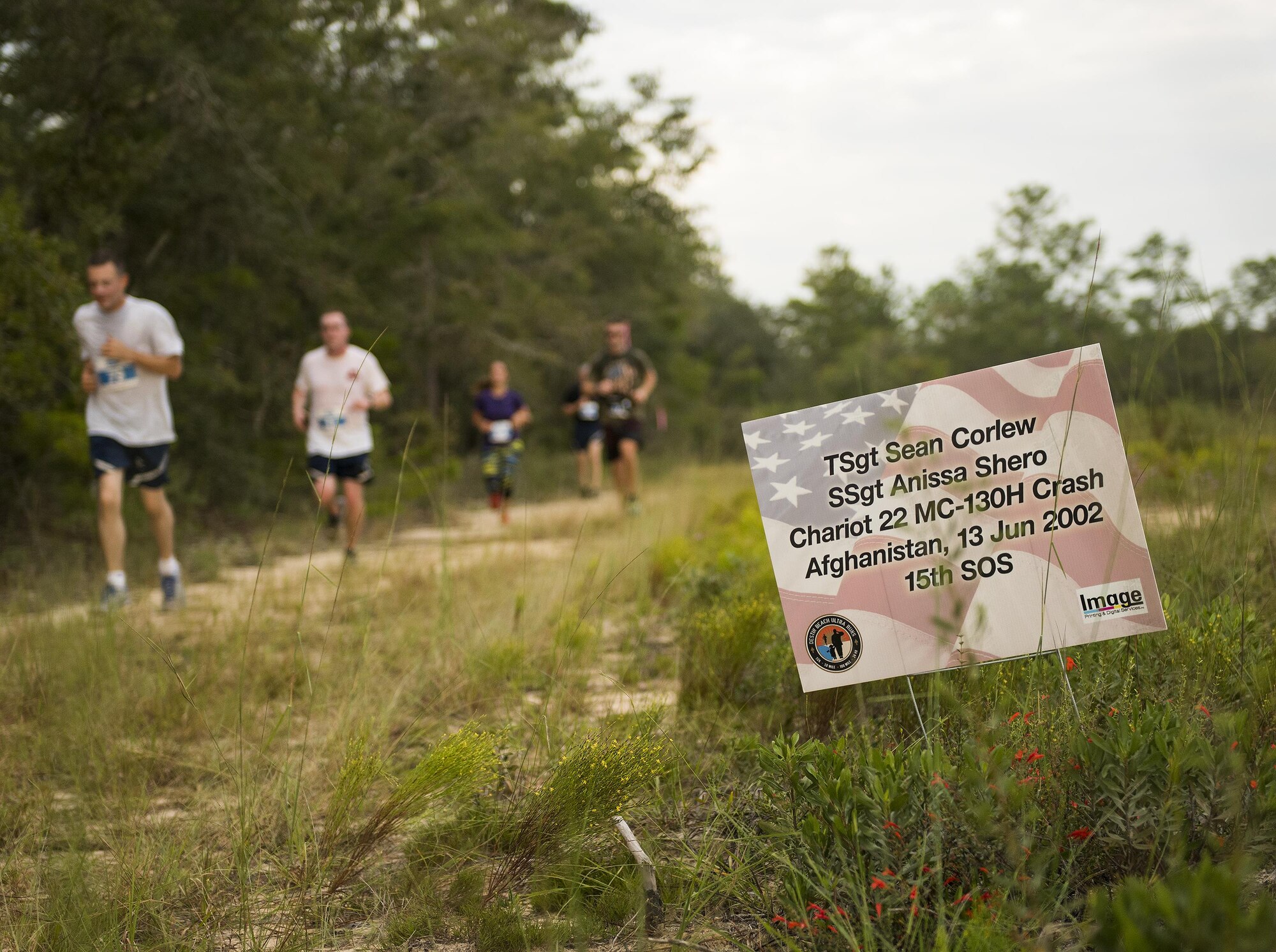 Runners move by a sign displaying the name of fallen Air Force special operator who lost his life after 9/11 during the Memorial 6k trail run Sept. 11 at Duke Field, Fla.  About 100 Airmen and families participated in the run.  (U.S. Air Force photo/Tech. Sgt. Sam King)