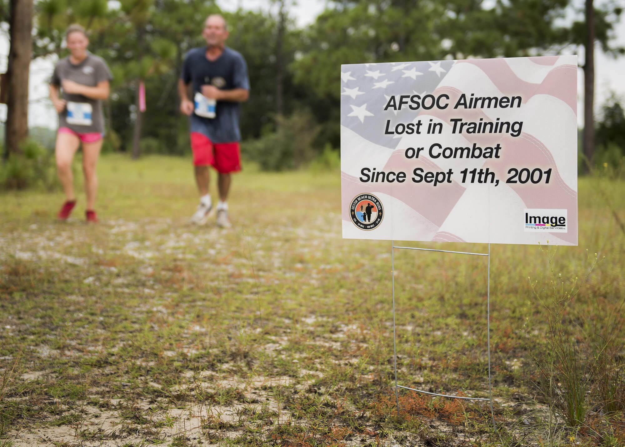 Runners move by a sign displaying the name of fallen Air Force special operator who lost his life after 9/11 during the Memorial 6k trail run Sept. 11 at Duke Field, Fla.  About 100 Airmen and families participated in the run.  (U.S. Air Force photo/Tech. Sgt. Sam King)