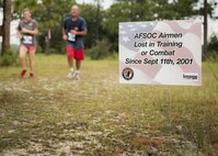Runners move by a sign displaying the name of fallen Air Force special operator who lost his life after 9/11 during the Memorial 6k trail run Sept. 11 at Duke Field, Fla.  About 100 Airmen and families participated in the run.  (U.S. Air Force photo/Tech. Sgt. Sam King)