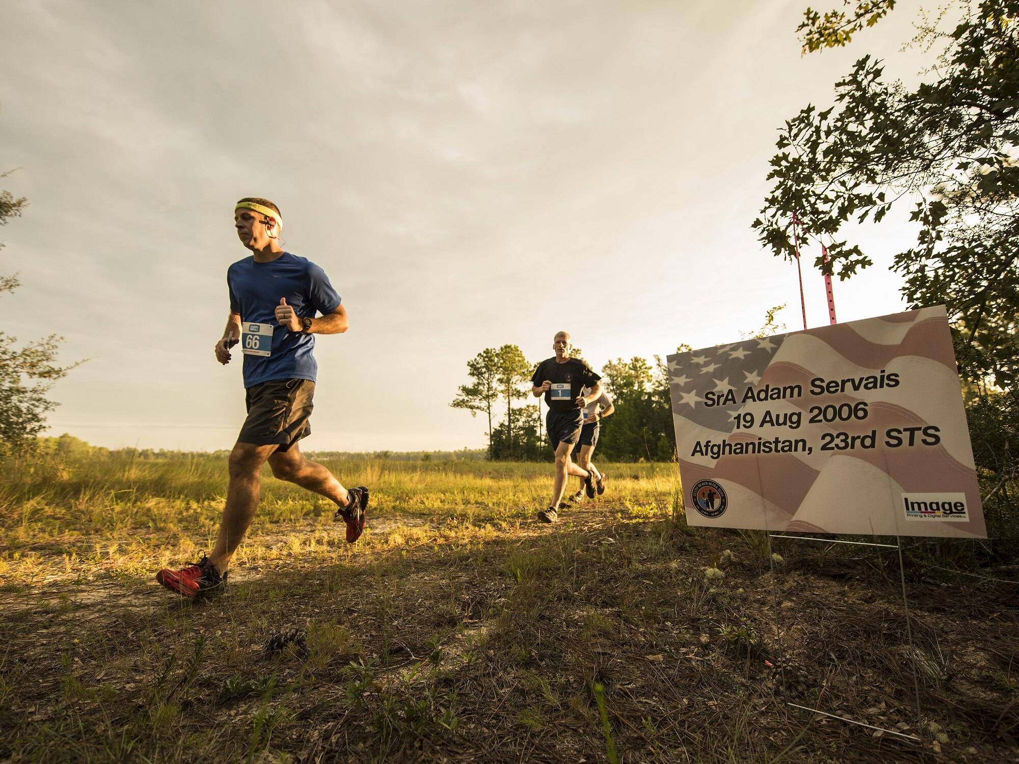 Runners move by a sign displaying the name of fallen Air Force special operator who lost his life after 9/11 during a Memorial 6k trail run Sept. 11 at Duke Field, Fla.  About 100 Airmen and families participated in the run.  (U.S. Air Force photo/Tech. Sgt. Sam King)