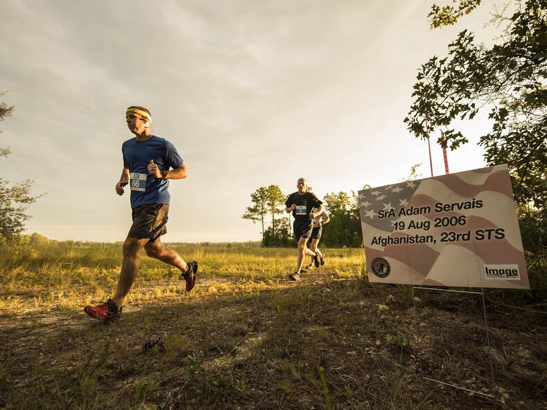 Runners move by a sign displaying the name of fallen Air Force special operator who lost his life after 9/11 during a Memorial 6k trail run Sept. 11 at Duke Field, Fla.  About 100 Airmen and families participated in the run.  (U.S. Air Force photo/Tech. Sgt. Sam King)