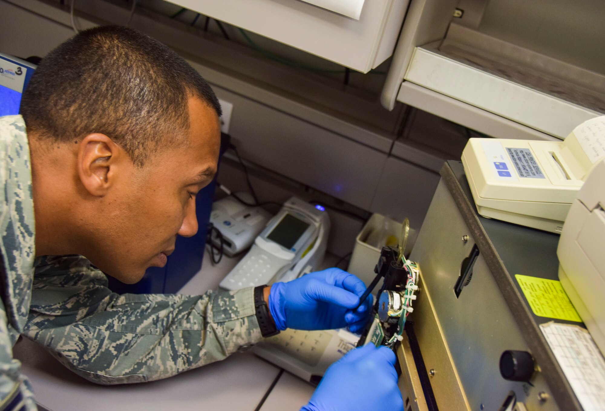 Tech. Sgt. Kristoffer Bruce, 379th Expeditionary Expeditionary Medical Operations Squadron biomedical equipment repair technician, has to done a pair of sterile gloves to work on a blood analyzer Sept. 8, 2016, Al Udeid Air Base, Qatar. He was checking for loose connections and broken wiring on the machine and  must wear the gloves to prevent  passing or catching contaminants.  (U.S. Air Force photo/Tech. Sgt. CarlosJ. Treviño/Released)