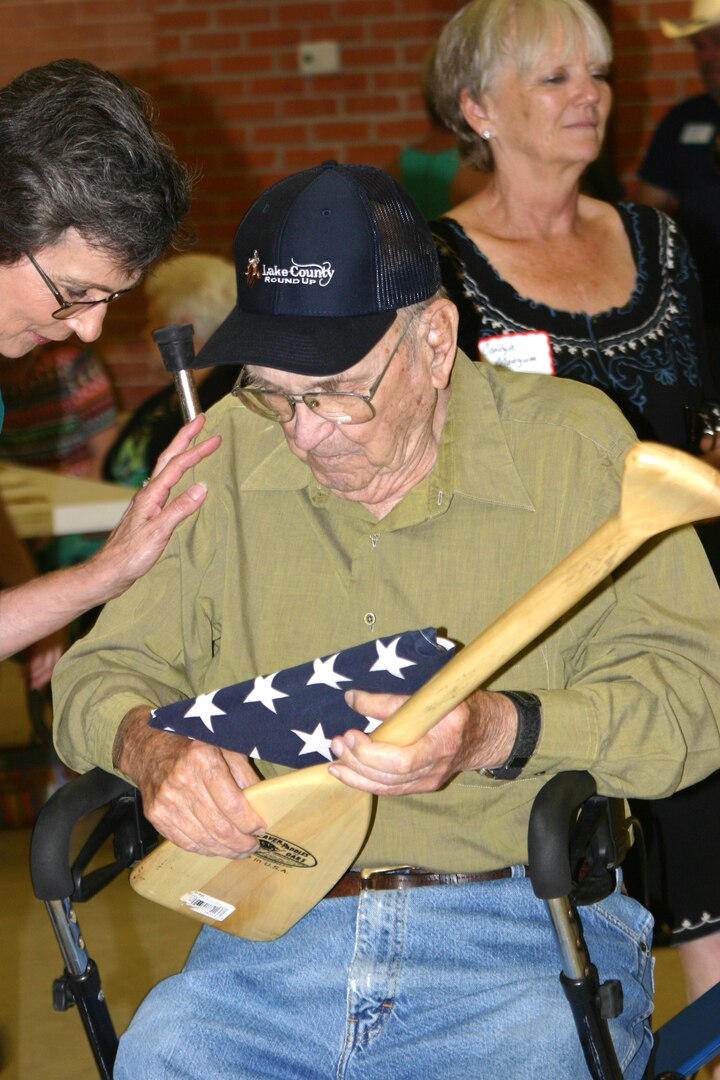 Navy veteran Tom Littleton admires the American flag and paddle presented to him on his 100th birthday from of Navy Recruiting District San Antonio recruiters in Devine, Texas, Aug. 27. Littleton served as a machinist's mate during World War II.