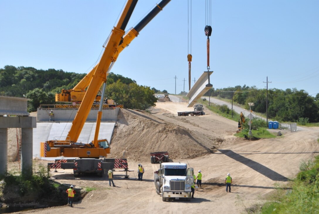 Crane operators complete the placement of a concrete beam which is part of the 350-foot bridge that will span House Creek in Fort Hood, Texas.