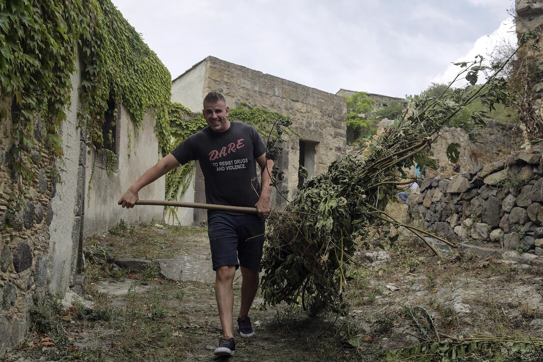 Lance Cpl. Chuck Lacosta, a basic landing support specialist with Special Purpose Marine Air-Ground Task Force Crisis Response-Africa, carries a pile of dead branches with a pitchfork in Vizzini, Sicily, Sept. 7, 2016.  Marines volunteered to clean up a local historic site and build fences during a community relations project.  (U.S. Marine Corps photo by Cpl. Alexander Mitchell/released)