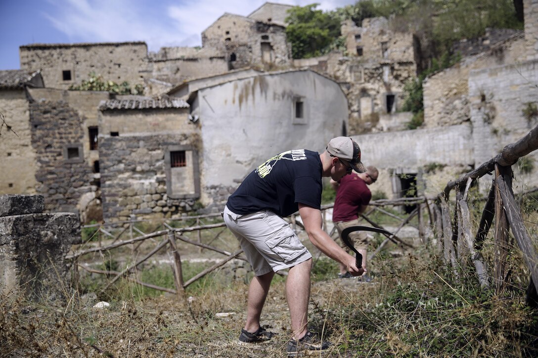 Cpl. Adam Crose, a generator mechanic with Special Purpose Marine Air-Ground Task Force Crisis Response-Africa, cuts down weeds and overgrowth with a sickle in Vizzini, Sicily, Sept. 7, 2016.  Marines volunteered to clean up a local historic site and build fences during a community relations project.  (U.S. Marine Corps photo by Cpl. Alexander Mitchell/released)