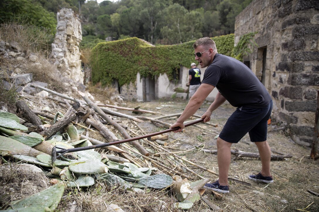 Lance Cpl. Chuck Locasto, a basic landing support specialist with Special Purpose Marine Air-Ground Task Force Crisis Response-Africa, racks up dead cactuses on a path in Vizzini, Sicily, Sept. 7, 2016.  Marines volunteered to clean up a local historic site and build fences during a community relations project.  (U.S. Marine Corps photo by Cpl. Alexander Mitchell/released)