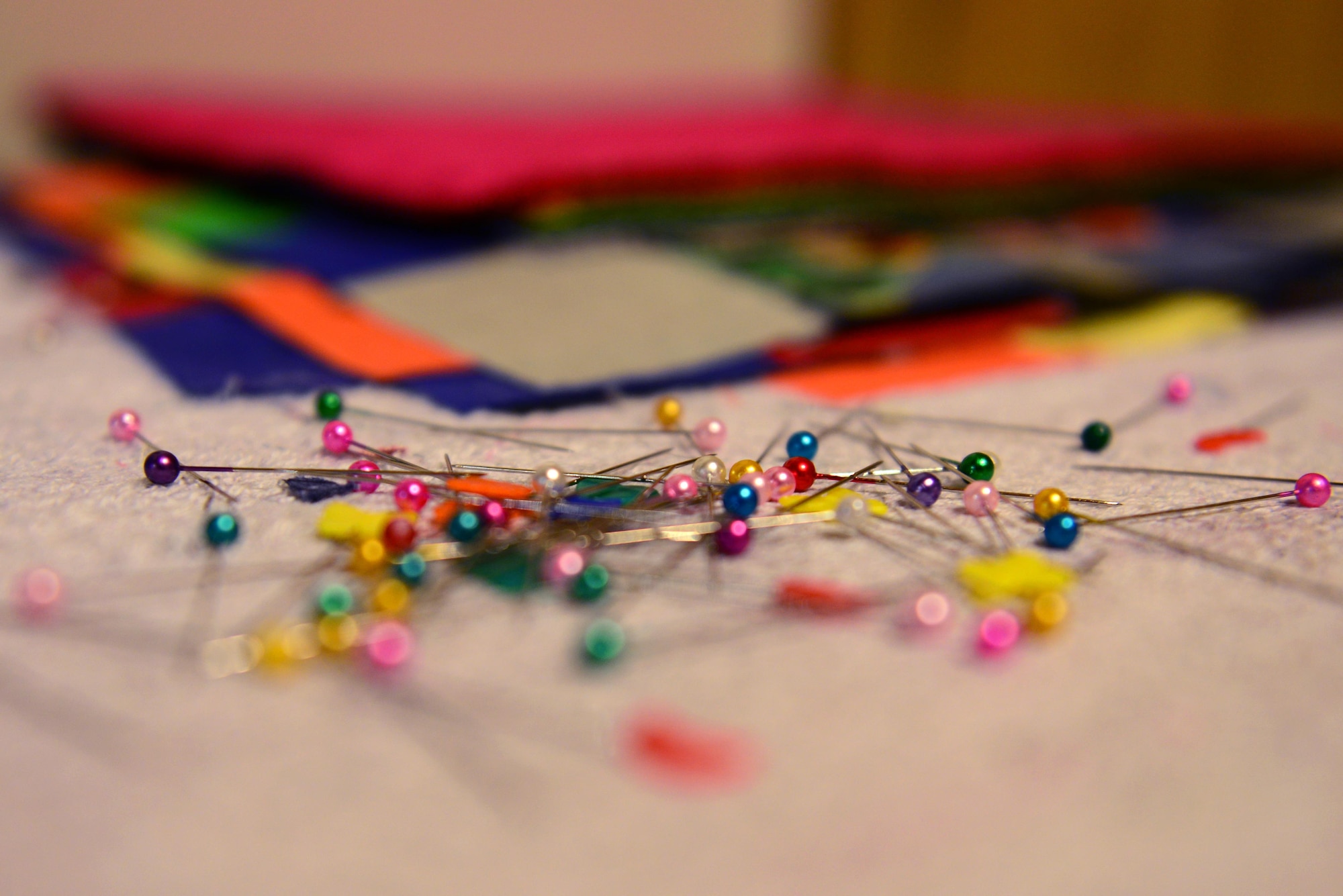 Pins sit in the foreground of a stack of fabric on an ironing table belonging to U.S. Air Force Senior Airman Karen Grinder, a 354th Contracting Squadron contracting administrator Sept. 13, 2016 at her home in North Pole, Alaska. The pins are used to hold pieces of fabric that need to be sewn together for quilts. (U.S. Air Force photo by Airman 1st Class Cassandra Whitman)