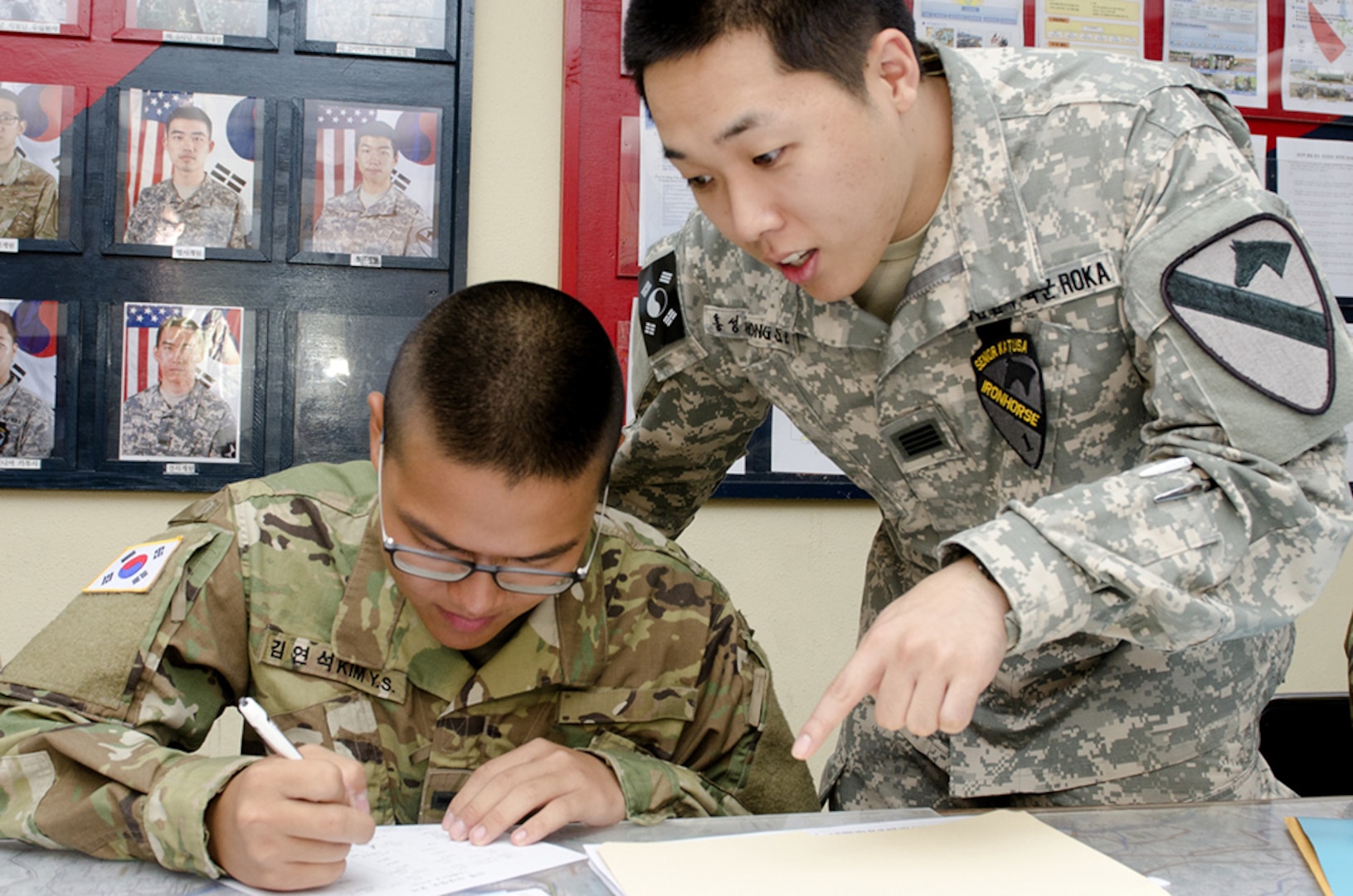 Sgt. Sung-Pyo Hong, a senior Korean Augmentation to the United States Army Soldier from Headquarters and Headquarters Company, 1st Armored Brigade Combat Team, 1st Cavalry Division, shows Pvt. Yeon-Seok Kim, a new KATUSA to the company, how to fill out personnel records, Sept. 1, 2016, at the Republic of Korea Army Support Office at Camp Hovey. Kim has been assigned to the brigade's ROKA Support Office as a human resources specialist. 