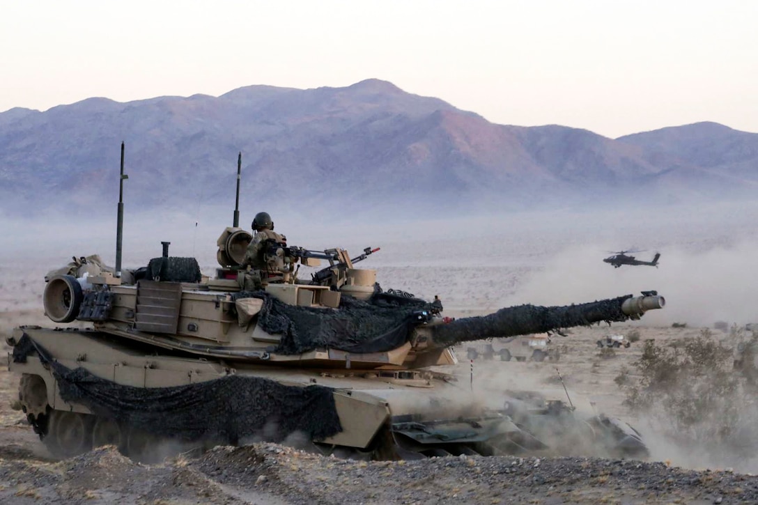 Soldiers maneuver in an M1A1 Abrams tank as an AH-64 Apache helicopter provides aerial security during exercise Decisive Action Rotation at Fort Irwin, Calif., Sept. 6, 2016. The soldiers are assigned to the 4th Infantry Division’s 3rd Brigade Combat Team. Army photo by Pfc. Michael Crews