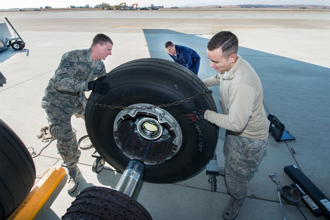 Air Force Staff Sgt. Elliott Bullis and Senior Airman Joseph Eidson guide a KC-10 Extender tire as Air Force Chief Master Sgt. Steve Nichols, center, command chief of the 60th Air Mobility Wing, lifts it using an aircraft wheel dolly during the "Works With Airmen" program at Travis Air Force Base, Calif., Sept. 9, 2016. The wheel dolly enables the airmen to lift and move the KC-10's 485-pound tires. Air Force photo by Louis Briscese