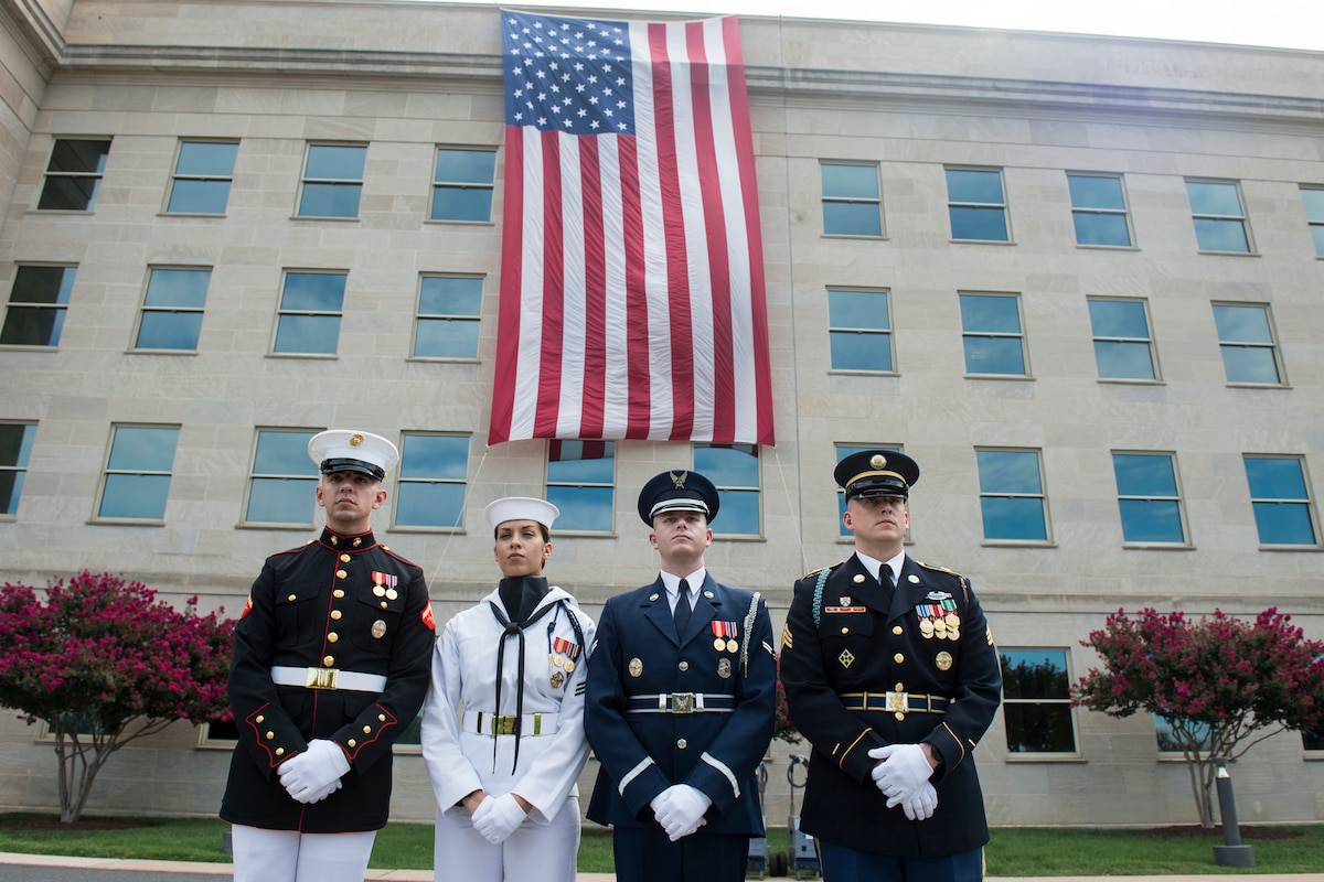 Service members stand before the American flag draping the Pentagon.