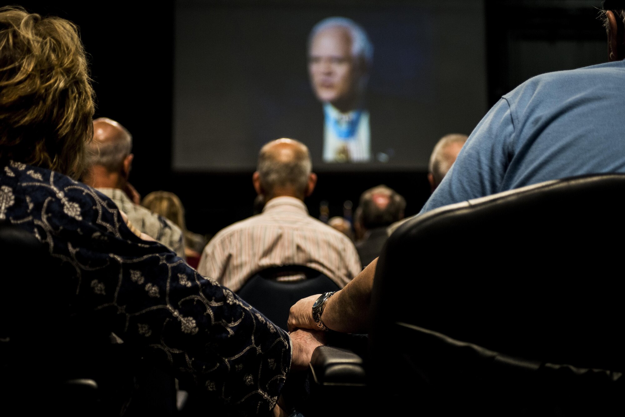 A couple holds hands while listening to video recalling a rescue mission during the Green Hornet Dedication ceremony at the National Museum of the United States Air Force near Wright-Patterson Air Force Base, Ohio, Sept. 15, 2016. The Green Hornets’ rescue mission earned the crew numerous awards including one member who received the Congressional Medal of Honor. (U.S. Air Force photo by Senior Airman Luke Kitterman/Released)