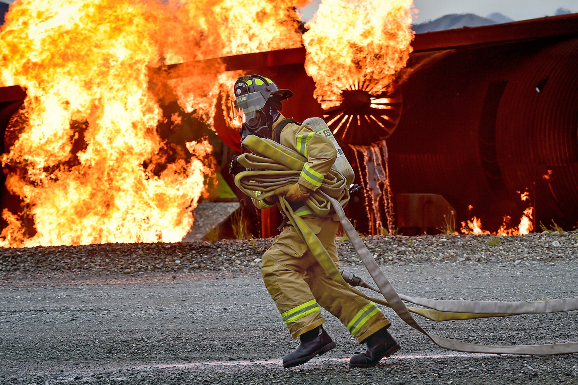 A fire protection specialist Airman assigned to the 673rd Civil Engineer Squadron runs hose lines during firefighter training on a simulated aircraft fire at Joint Base Elmendorf-Richardson, Alaska, Wednesday, Sept. 14, 2016.  Aircraft live fire training is conducted periodically throughout the year at JBER to ensure Airmen are prepared to combat aircraft fuel fires.