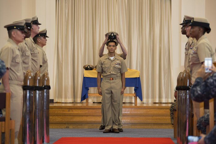 U.S. Navy Chief Petty Officer Johnerikson Angeles, chief aviation machinist mate with Aircraft Intermediate Maintenance Detachment, stands at attention as his cover is placed on his head during a promotion ceremony in the Marine Memorial Chapel at Marine Corps Air Station Iwakuni, Japan, Sept. 16, 2016. Signifying a history of tradition, placing the cover on the Sailor’s head finalizes their promotion and welcomes them into the ranks of chief petty officers. (U.S. Marine Corps photo by Lance Cpl. Joseph Abrego)