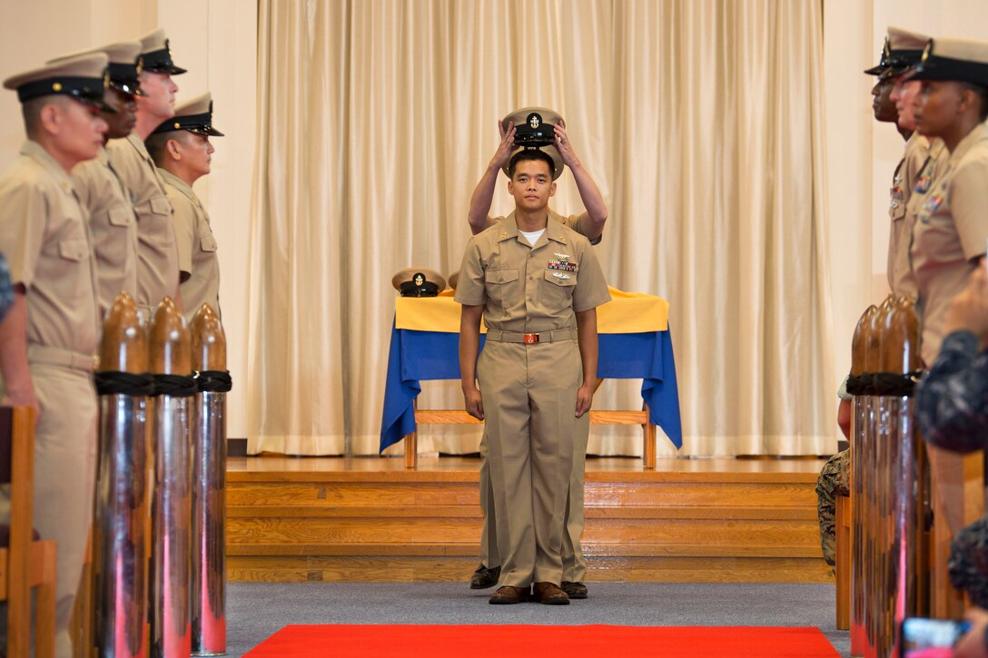Newly promoted Navy Chief Petty Officer Johnerikson Angeles, center, stands at attention as the khaki cover of a chief petty officer is placed on his head during a pinning ceremony in the Marine Memorial Chapel at Marine Corps Air Station Iwakuni, Japan, Sept. 16, 2016. Angeles is a chief aviation machinist mate assigned to Aircraft Intermediate Maintenance Detachment. Marine Corps photo by Lance Cpl. Joseph Abrego